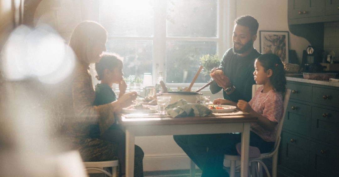 En familj med två barn som äter middag vid soligt matbord